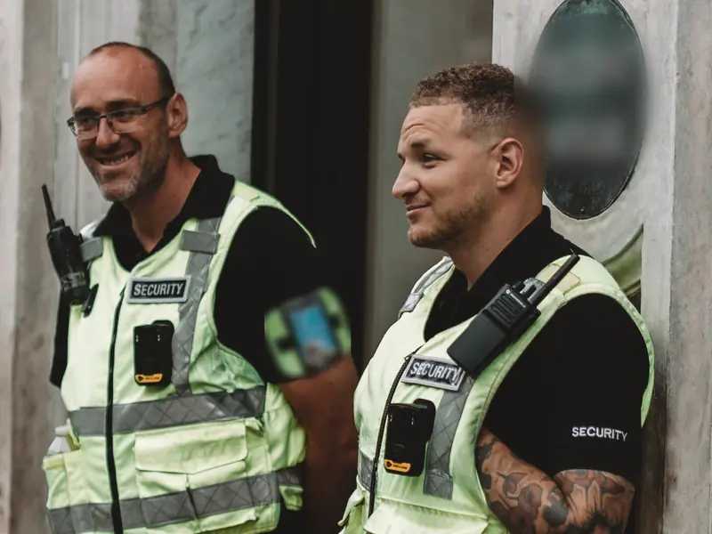 Two smiling security officers in high-visibility vests at a building entrance